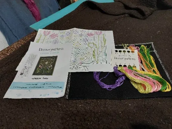 Buyer photo of the Tulip kit unboxed: black fabric, color chart pages and a Dream pattern card holding purple, pink and green threads