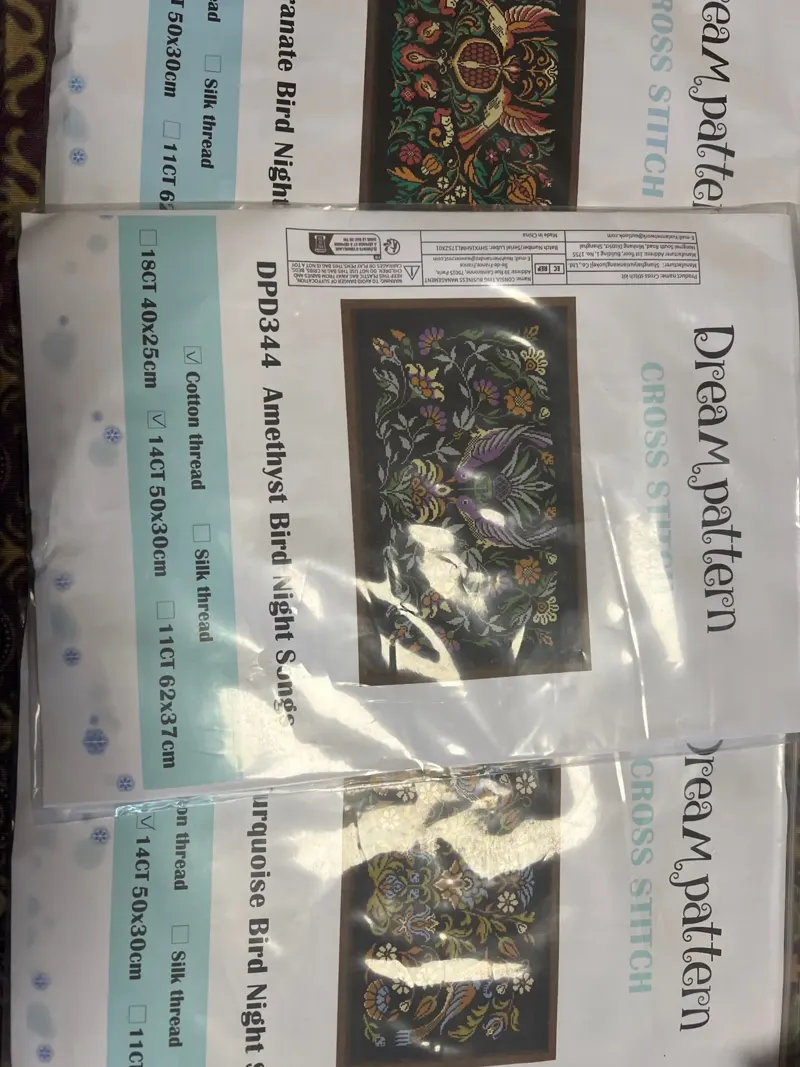 Buyer photo of three Night Songs kit packets: the Amethyst, Pomegranate and Turquoise bird designs on black fabric